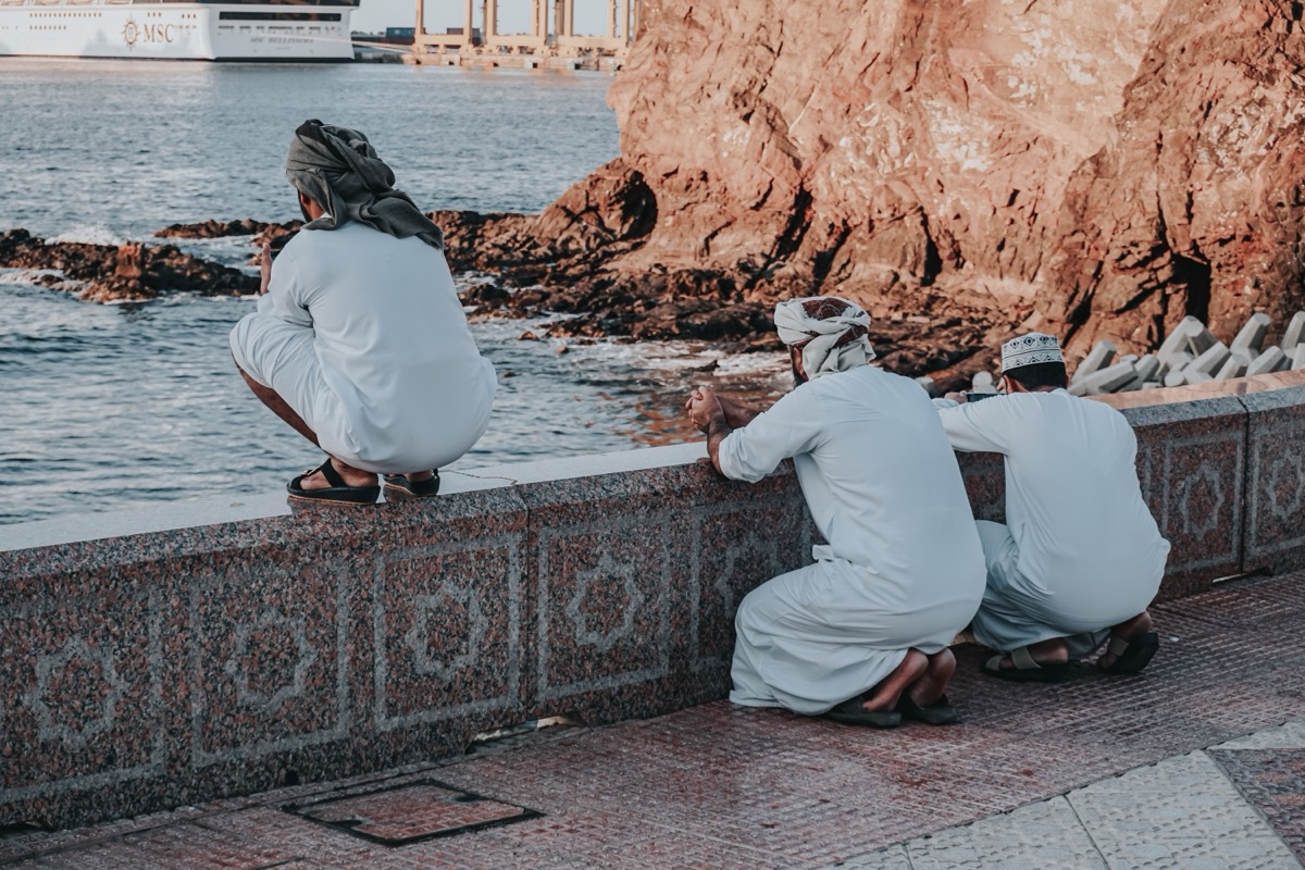 Men resting on the Muttrah Corniche seawall watching a cruise ship