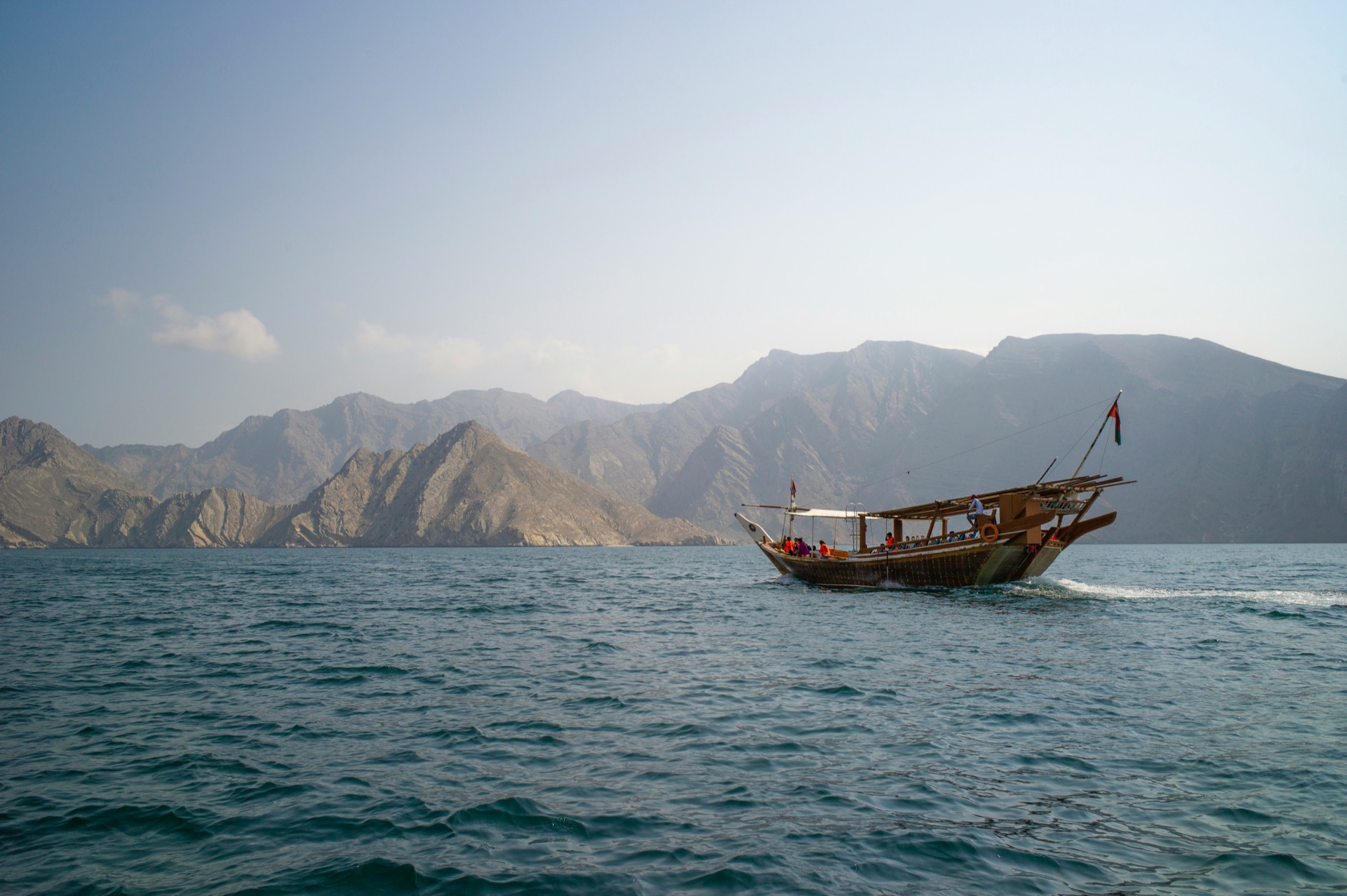 Traditional dhow boat sailing along Oman's mountainous coastline